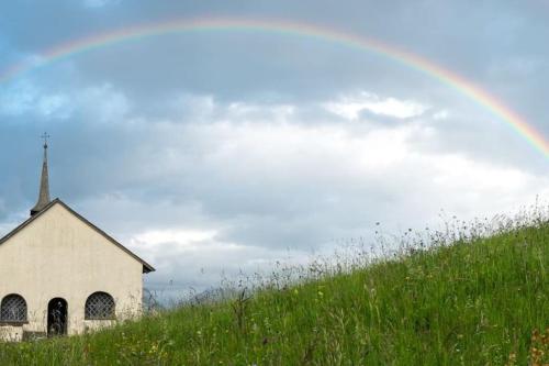 Ein Regenbogen über einer alten Kirche auf einem Hügel in der Unterkunft Komplettes Hotel mit 10 Zimmern in Bad Ragaz