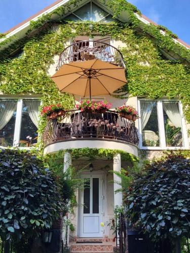 a house with a balcony with an umbrella at Vila Florena Garden in Palanga