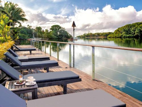 a deck with chairs and tables next to a river at Novotel Suva Lami Bay in Suva