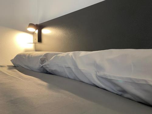 a bed with white sheets and a light on the wall at San Valentino House in Bussolengo