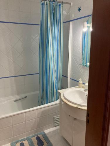 La salle de bains est pourvue d'un rideau de douche bleu et d'un lavabo. dans l'établissement Apartamento Vila Nova 1, à Armação de Pêra