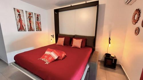1 dormitorio con 1 cama con sábanas y almohadas rojas en Le Sea-Breeze - Beau studio piscine VUE LAGON, en Marigot