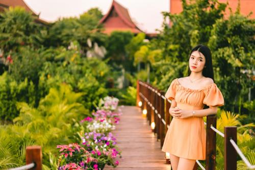 a woman in an orange dress walking down a wooden bridge at Nakara Villas & Glamping Udon Thani in Udon Thani