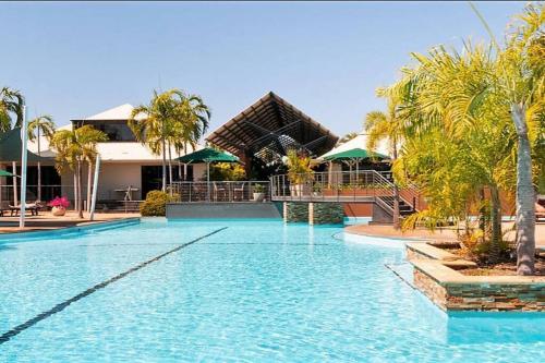 a large swimming pool with palm trees and a building at Modern 2 Bed Apartment - Oaks Resort, Cable Beach in Cable Beach