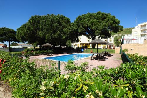 a swimming pool with tables and umbrellas and trees at Caparica Sun Centre in Costa da Caparica