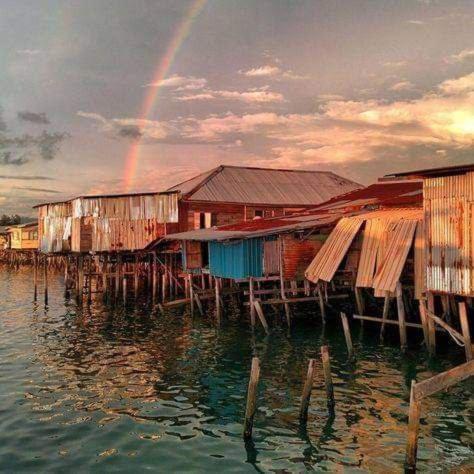 a rainbow over a group of houses on the water at Lovely & Cozy Apt In Nature City in Sandakan