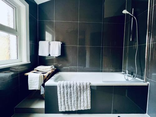 a bathroom with a bath tub with black tiles at Neils Place hosted by AirOperate in London