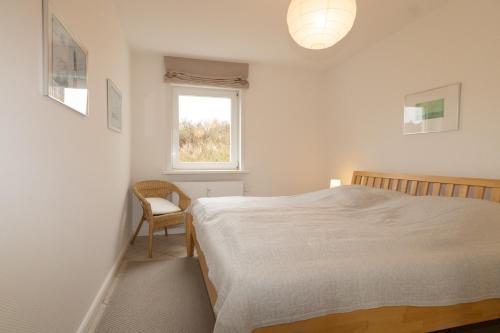 a bedroom with a bed and a chair and a window at Ferienwohnung Strandrose in Hörnum