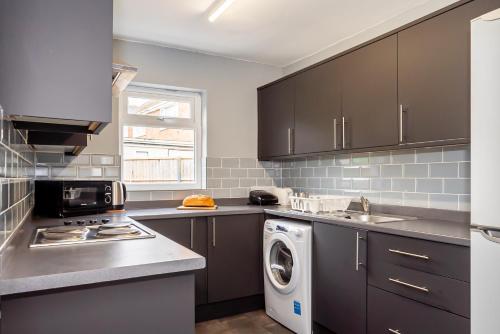 a kitchen with gray cabinets and a washer and dryer at Shirley House 3, Guest House, Self Catering, Self Check in with Smart Locks, Use of Fully Equipped Kitchen, close to City Centre, Ideal for Longer Stays, Walking Distance to BAT, 20 min Drive to Fawley Refinery, Excellent Transport Links in Southampton