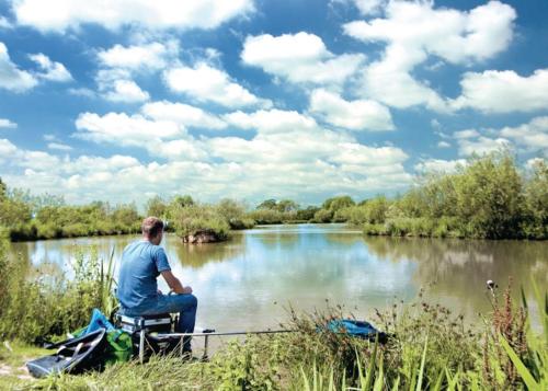 a man sitting on a chair next to a river at Goodiford Mill Lakes in Kentisbeare