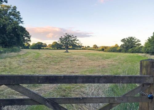 a wooden fence in a field with a tree at Goodiford Mill Lakes in Kentisbeare