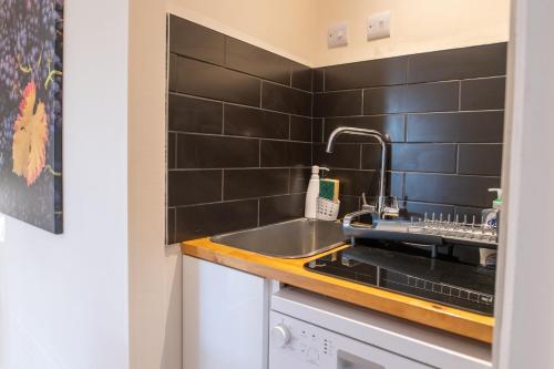 a kitchen with a sink and black tiled walls at Terlingham Lane Cottage in Folkestone