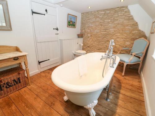 a bathroom with a white bath tub and a chair at Holly Cottage in Minster Lovell