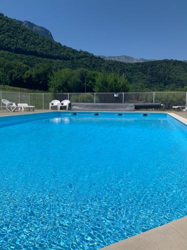 a large blue swimming pool with two chairs and mountains at Petit cocon entre lac, golf et montagne, proche d'Annecy in Giez