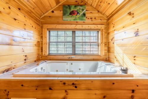 a soaking tub in a wooden room with a window at Comfort Cabin Bearway To Heaven w Private Hot Tub in Pigeon Forge