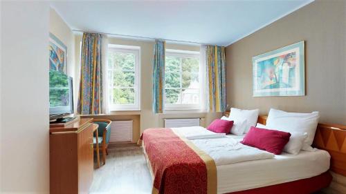 a bedroom with a bed and a desk and windows at Hotel Alt Montjoie in Monschau