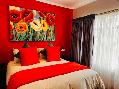 a red bedroom with a bed with red pillows and a painting at @ Home Bed & Breakfast in Brakpan