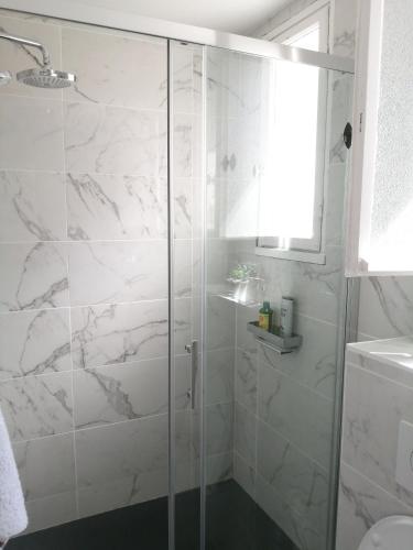 La salle de bains est pourvue d'une douche et de carrelage en marbre blanc. dans l'établissement Studio confortable à Guéthary 30 m² avec balcon relaxant, à Guéthary