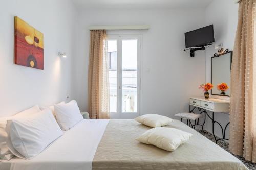a bedroom with a white bed with a desk and a window at Marialena Rooms in Skopelos Town