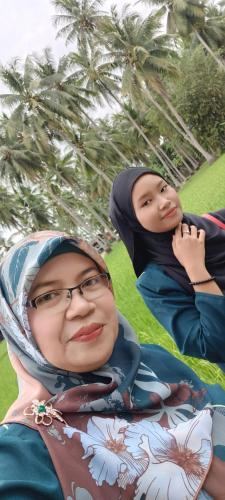 two women sitting on the grass with palm trees in the background at Homestay Damai Sri Kota in Kepala Batas
