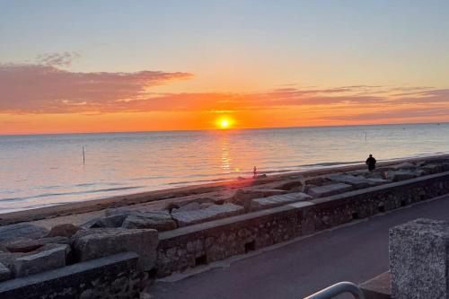 eine Person, die am Strand steht und den Sonnenuntergang beobachtet in der Unterkunft Studio dans le centre près de la mer in Agon Coutainville
