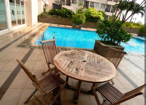 uma mesa de madeira e cadeiras ao lado de uma piscina em MARGONDA RESIDENCE 3 em Kemirimuka Dua
