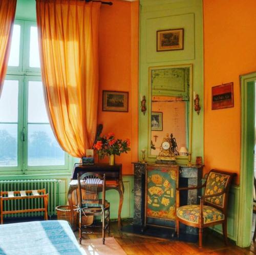 a bedroom with an orange wall with a mirror and chairs at Chateau du Fraisse in Nouic