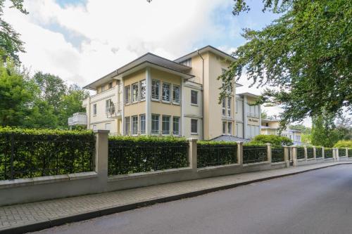 ein gelbes Haus mit einem Zaun vor einer Straße in der Unterkunft Villa Charlotte App.13 in Heringsdorf