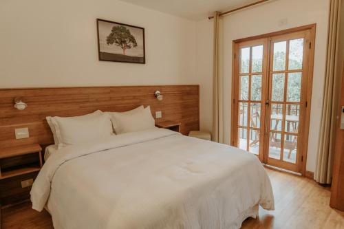 Un dormitorio con una gran cama blanca y una ventana en La Brume Pousada, en Campos do Jordão