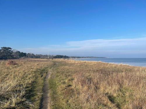 a dirt road through a field with the ocean at Hyggeligt og lyst feriehus nær stranden i Klint in Nykøbing Sjælland