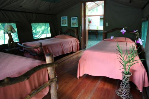 a bedroom with two beds and a vase with flowers at Rafiki Safari Lodge in Savegre