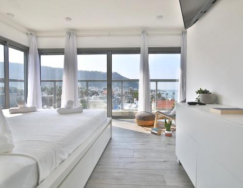 een slaapkamer met een wit bed en een groot raam bij Bat-Galim Beach Apartment in Haifa