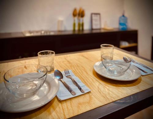 a wooden table with two plates and glasses and silverware at Casa Ceiba/Dpto. entero cerca del Centro Histórico in Oaxaca City