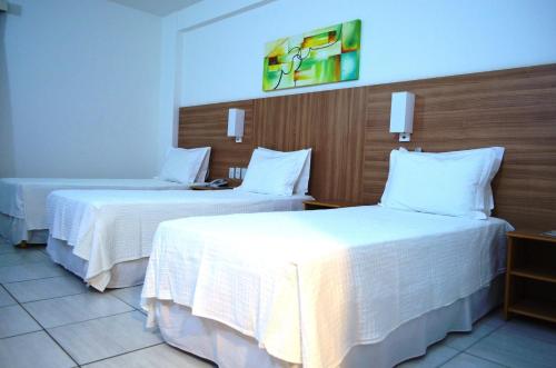 two beds in a hotel room with white sheets at Hotel Áster in Alagoinhas