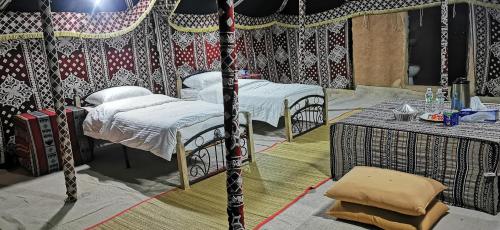a room with two beds in a tent with a table at Desert Wonders Camp in Ḩawīyah