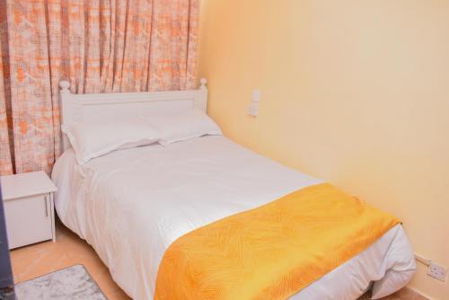 Dormitorio pequeño con cama blanca y manta amarilla en Leshi Place, Kinoru - Makutano, Meru, en Meru