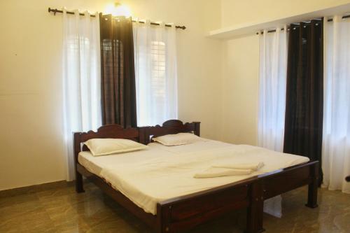 a bedroom with a bed with white sheets and windows at RIO CASA , Private villa in soochipara in Meppādi