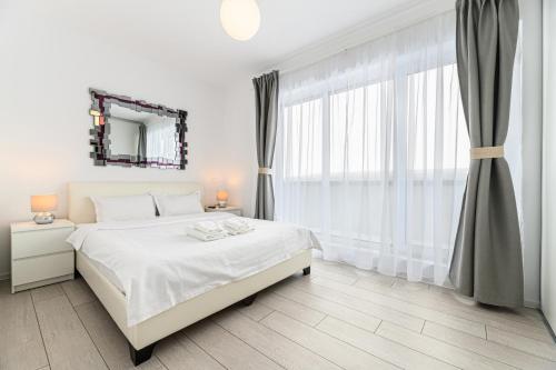 a white bedroom with a bed and a large window at Nubia Apartment in Braşov