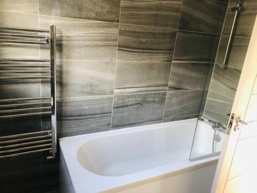 a bathroom with a white tub and a tiled wall at Diamond accommodation in London