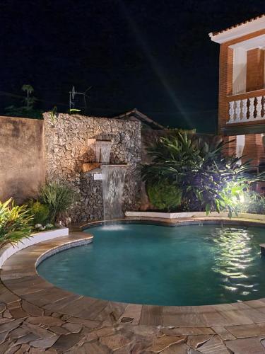 a pool with a waterfall in a backyard at night at Estação Brotense - Casa com piscina e fogueira exclusiva in Brotas