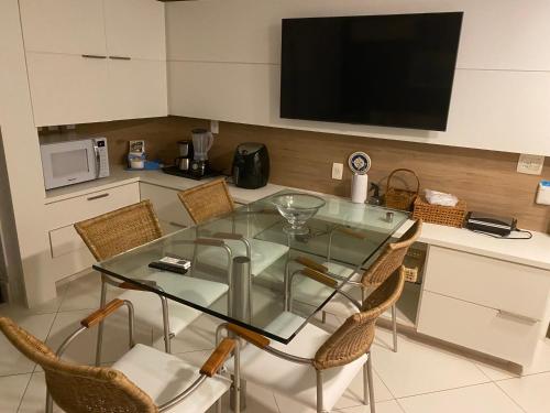 a kitchen with a glass table with chairs and a tv at Flat Beach Class Resort Muro Alto in Porto De Galinhas