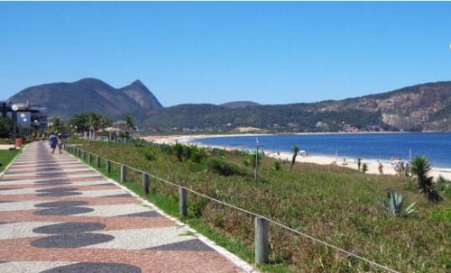 a walkway next to a beach with mountains in the background at Camboinhas LOFT Temporada in Niterói