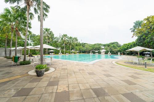 una grande piscina con palme e ombrelloni di RedLiving Apartemen Aeropolis - Ivan Tower AR1 a Tangerang
