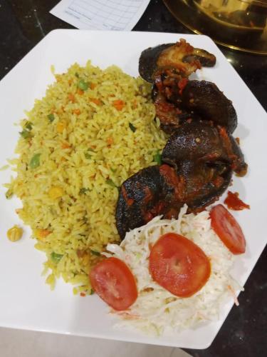 a plate of food with rice and meat and tomatoes at Kawruky Hotel Benin in Benin City