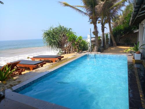 a swimming pool next to a beach with palm trees at Asiri Yoga Retreat in Galle