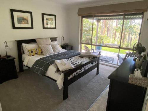a bedroom with a bed and a large window at Bimbimbie House Batemans Bay in Surf Beach