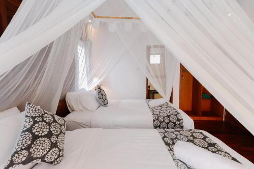 two beds in a room with white curtains at The Lavana Jhonny Kibung Villas Lembongan in Nusa Lembongan