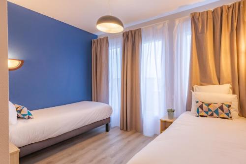 a bedroom with two beds and a blue wall at Appart'City Classic Caen in Caen