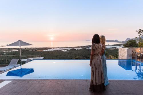 a woman standing by a swimming pool looking at the sunset at Falasarna Luxury Villas I Private "heated" pools, ideal for groups in Falasarna
