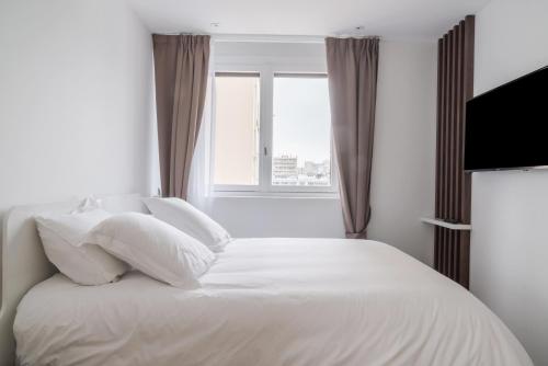 a white bed with white pillows and a window at Fauriel Paul - Appartement moderne et spacieux in Saint-Étienne